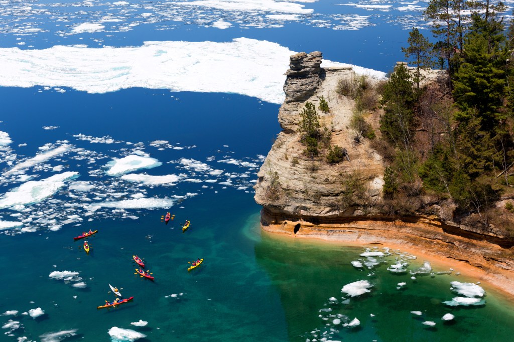Kayakers maneuver through ice floes to view Miners Castle rock formation on Lake Superior.